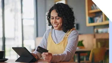 Smiling woman holds her credit card while looking at her ipad