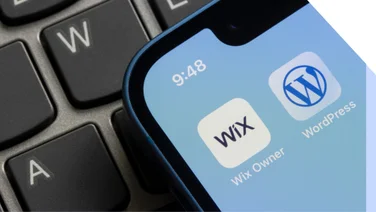 Phone on keyboard shows the Wix app and WordPress app side by side