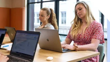 Two focused women working on laptops in a bright office environment