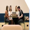 A group of four colleagues collaborating on a project with a laptop in an office environment.