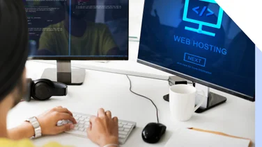 Person taps on keyboard in front of two desktop screens looking at web hosting