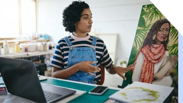 Creative woman gestures to her painting in front of her laptop