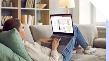 Photo of a woman lying down on a sofa browsing an online store on her lap