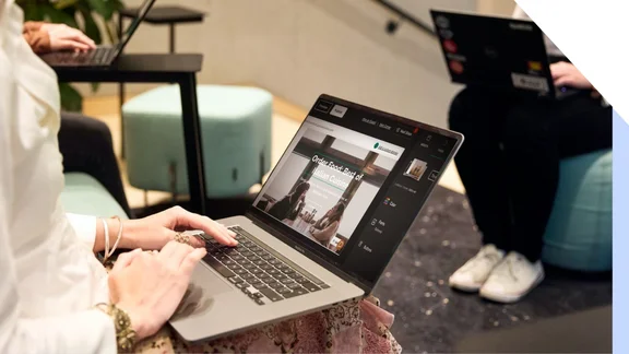 Two professionals working on laptops in a modern office setting, one is editing her website on GoDaddy's website builder.