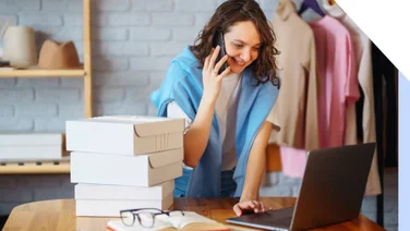 A woman on a laptop at her desk on the phone and with parcels