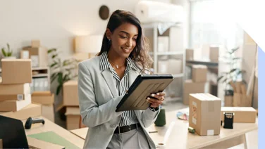 Smiling businesswoman works on a tablet surrounded by packing boxes