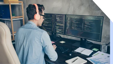 Rear view of a man working at two desktops coding