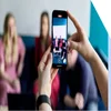 A close-up of a smartphone taking a video of friends for social media, with a blurred background.