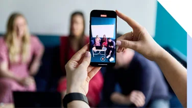 A close-up of a smartphone taking a video of friends for social media, with a blurred background.