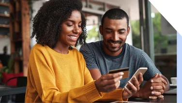 a woman holding a credit card and a phone with a man watching next to her