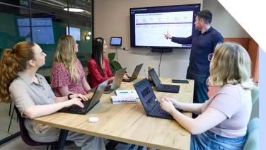 A group of professionals attending a presentation led by a confident presenter pointing at a screen displaying graphs.