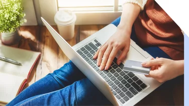 Laptop on lap with a hand holding a credit card