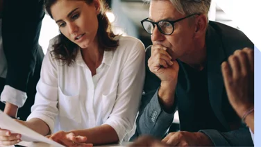 Man and woman sit at a desk looking thoughtful, discussing over sheets of paper