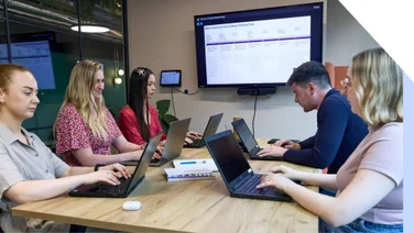 A group of professionals collaborating at a business meeting with laptops and presentation screen.