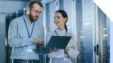 Two colleagues stand in data center holding laptop and smiling