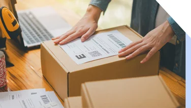 person attaching shipping label to a cardboard box on a table