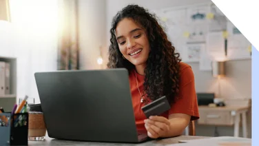 Photo of a woman at her laptop holding a credit card in her hand