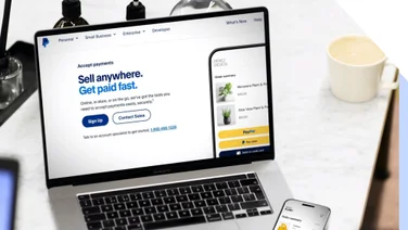 Laptop displaying PayPal's online payment options with a smartphone processing a transaction on the side.