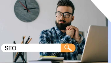 A man sat by his laptop thinking with a graphic overlay of "SEO" in a search bar
