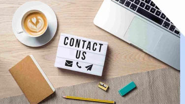 Desk with a "Contact Us" card in the center and notebook, laptop, coffee cup around it