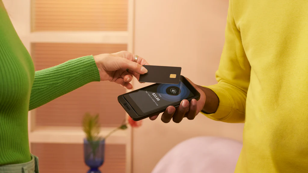 image of green jumper-wearing person tapping a card agaisnt a phone held my a person in a yellow jumper