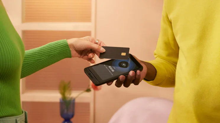 image of green jumper-wearing person tapping a card agaisnt a phone held my a person in a yellow jumper