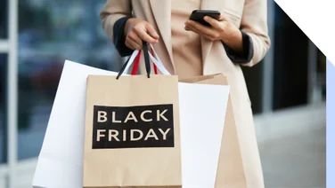 Person holds phone in one hand and bags saying Black Friday in the other