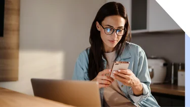 woman sits with an open laptop looking at her phone in her hand