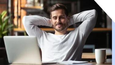 Man with arms behind his head relaxing as he looks at a laptop