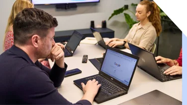 Man looks thoughtfully at the Google search on his laptop screen, as part of a business meeting with colleagues in an office.