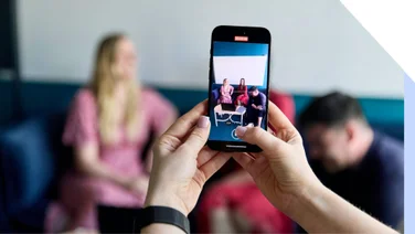 Person using a smartphone to photograph friends sitting across the table.
