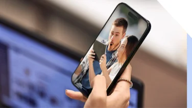 Hand holding smartphone, with an image of a comically surprised-looking couple on the screen.