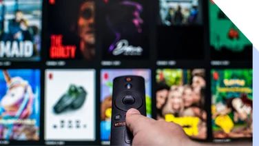Blurred image of Netflix's content with a hand holding a TV remote pointing at the screen
