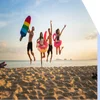 Four people in swimwear jump in the air on a sandy beach holding pool inflatables