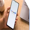 Hand holding a mobile with Google merchant center logo displayed on a white screen