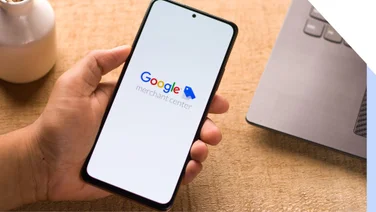 Hand holding a mobile with Google merchant center logo displayed on a white screen