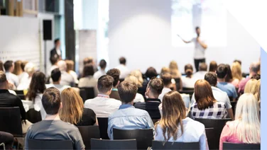 Audience of people sat in chairs listening to a speaker deliver a talk at a conference event