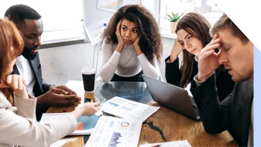 Group of people looking stressed around a work table as if trying to solve a problem