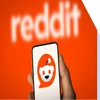 Hand holding a mobile showing a white background with the Reddit logo on, held against the red Reddit background