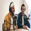 Two men sat a desk with podcast equipment in front of them and headphones on