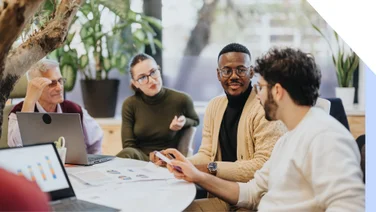Group of office workers chatting around a table with laptops and paper in front of them