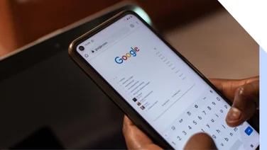 Hands holding a mobile device showing the Google homepage with a search query
