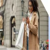 Woman in a coat standing outside with a couple of shopping bags while looking at her phone