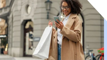 Woman in a coat standing outside with a couple of shopping bags while looking at her phone