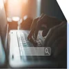Hands typing at a laptop with a floating image of a search bar on top