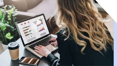 A woman typing on a laptop with graph data on the screen