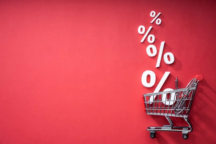 A shopping cart with percentage signs coming out of it against a plain background
