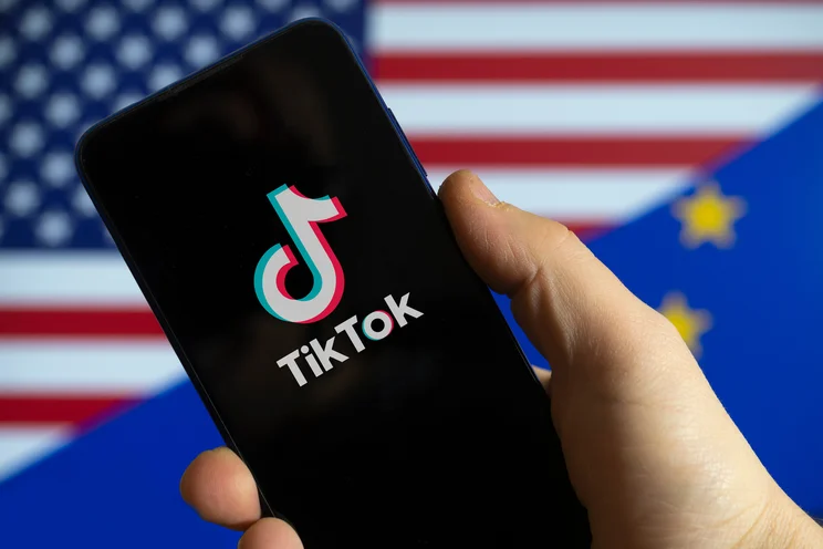 Phone with TikTok logo on the screen being held in front of an American flag