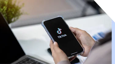 Hands holding a mobile showing the TikTok logo on the screen