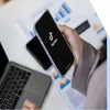 A phone with TikTok logo held above a table with a laptop on